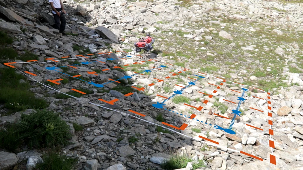 A delimited scree plot photographed from above, with the survey grid in orange and the robot's waypoint path in blue superimposed on it.
